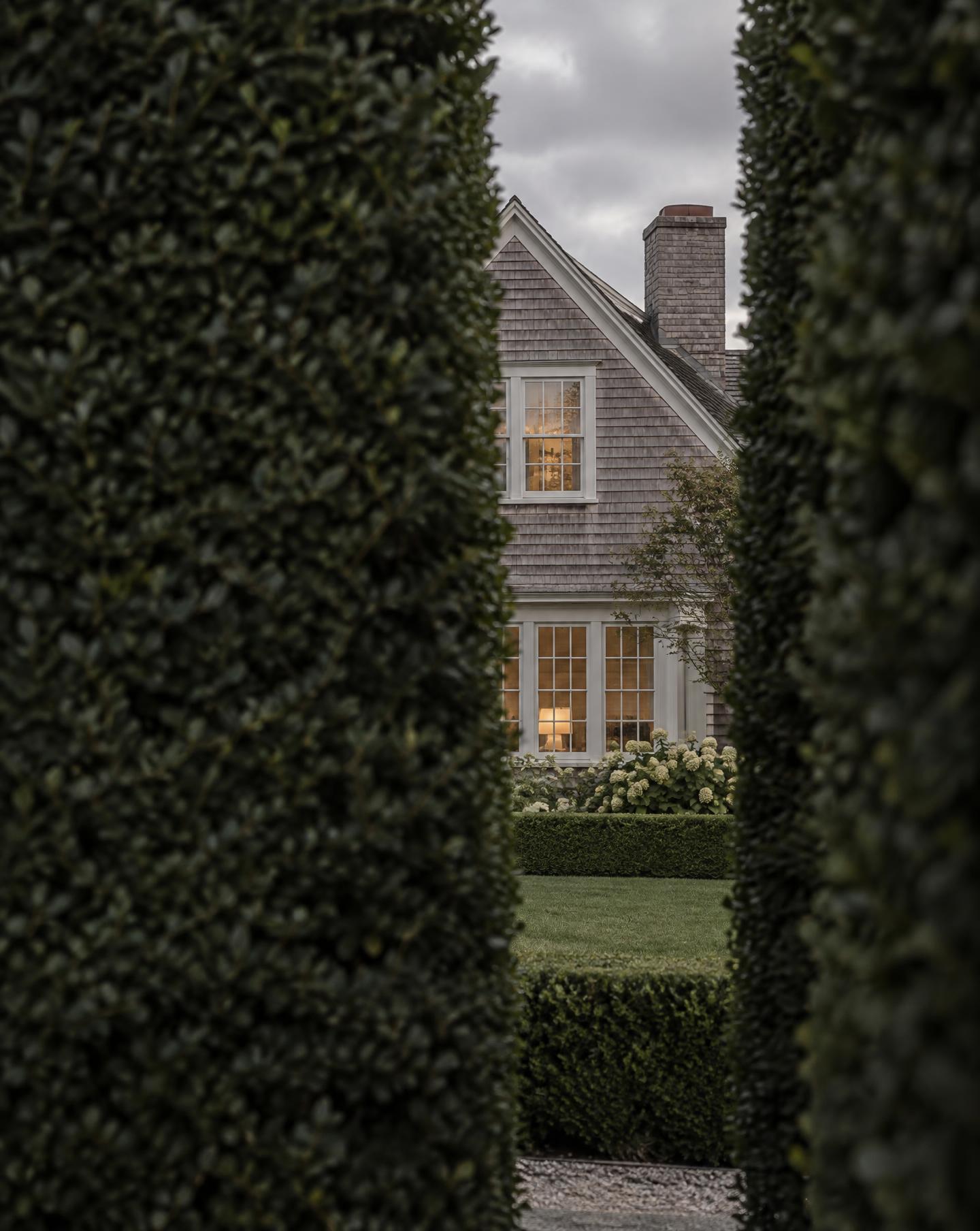 Classic shingled residence glimpsed through a clipped privet hedge — an editorial metaphor for protected client privacy